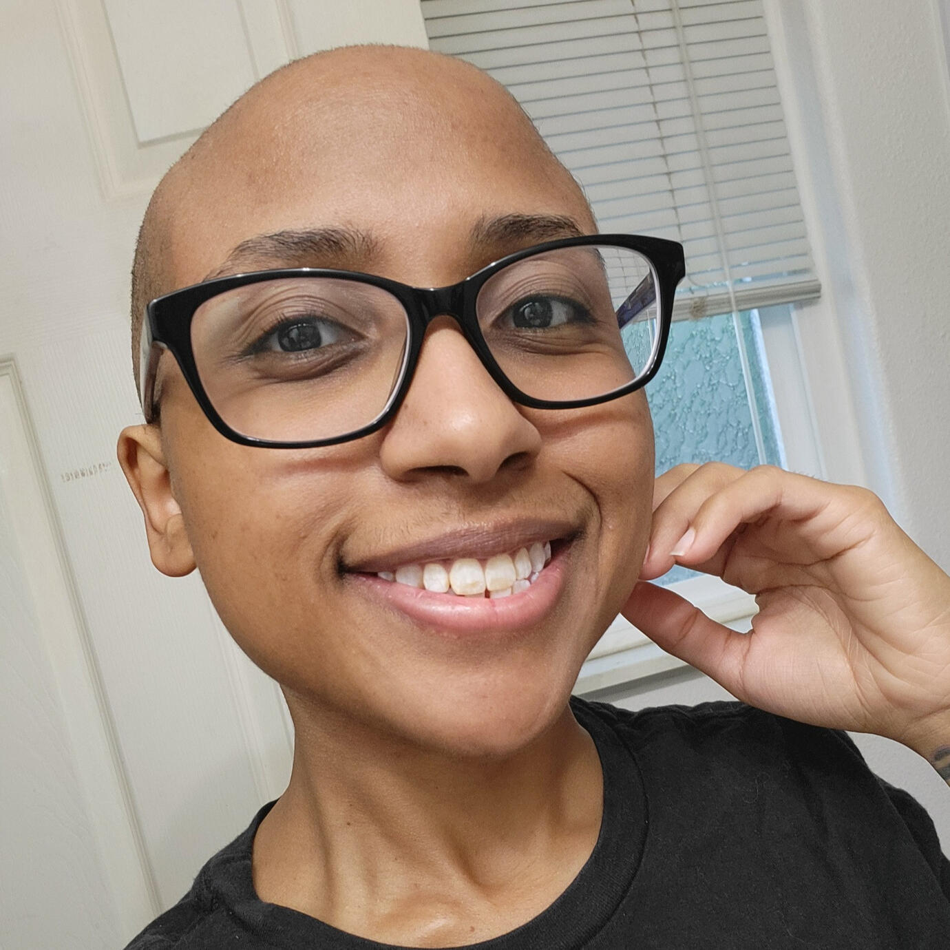 AmethystMoon smiling at the camera. She has a bald head and is wearing glasses.