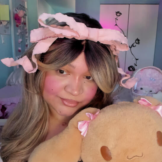 softestfairie holding a lovelymocha stuffed animal, and wearing a very large pink curly bow headband.