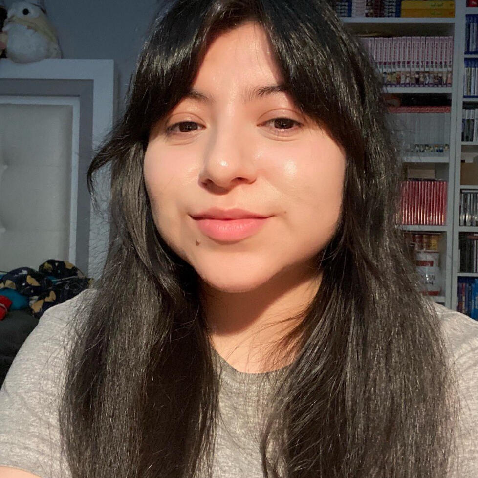 Selfie of femme presenting person with long hair, smiling and wearing a textured blouse.